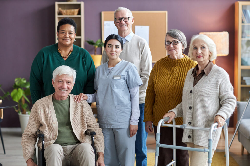 Diverse group of senior people looking at camera in retirement home while posing with nurse all smiling